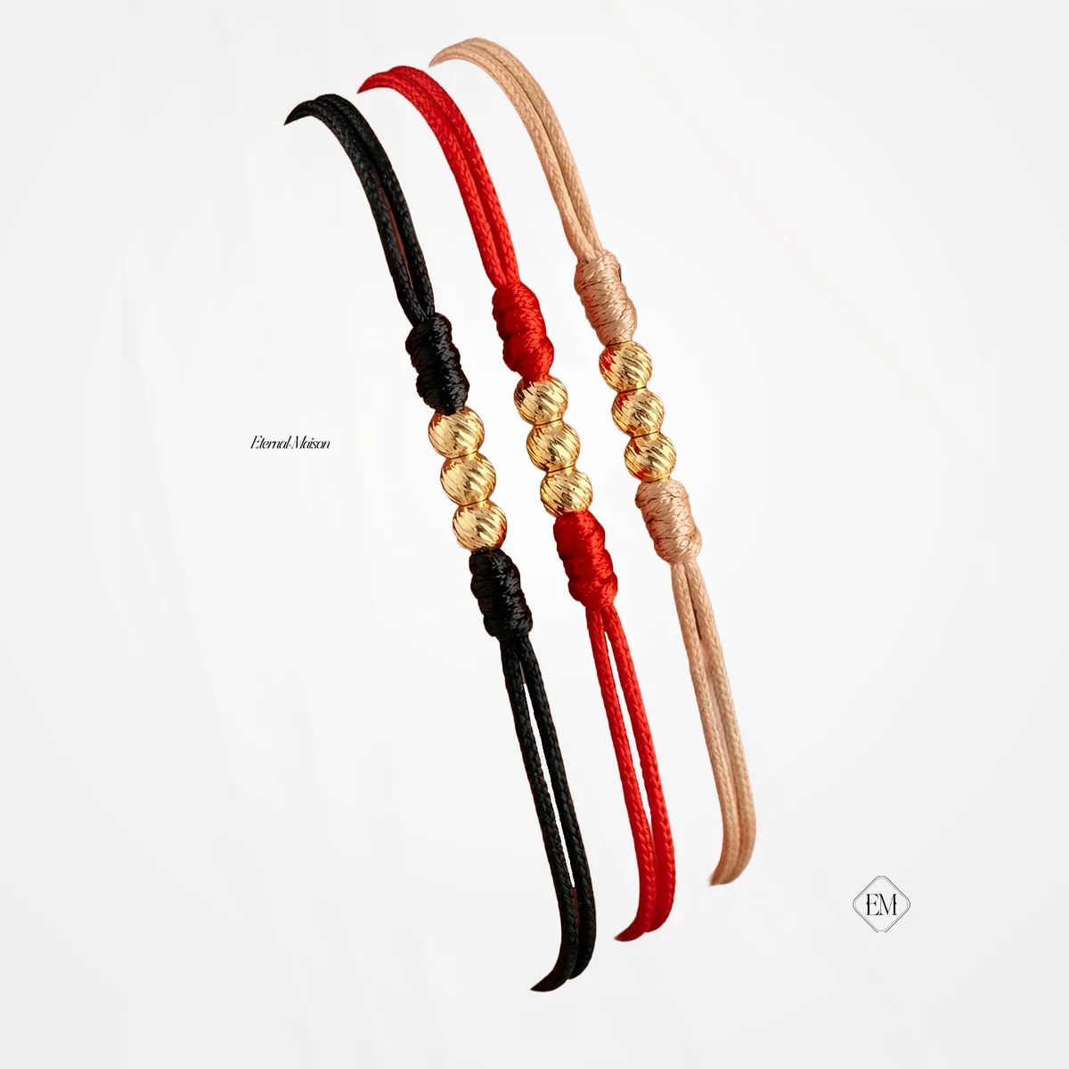 Tres pulseras de cordón negro, rojo y beige, cada una con tres balines diamantados en oro.