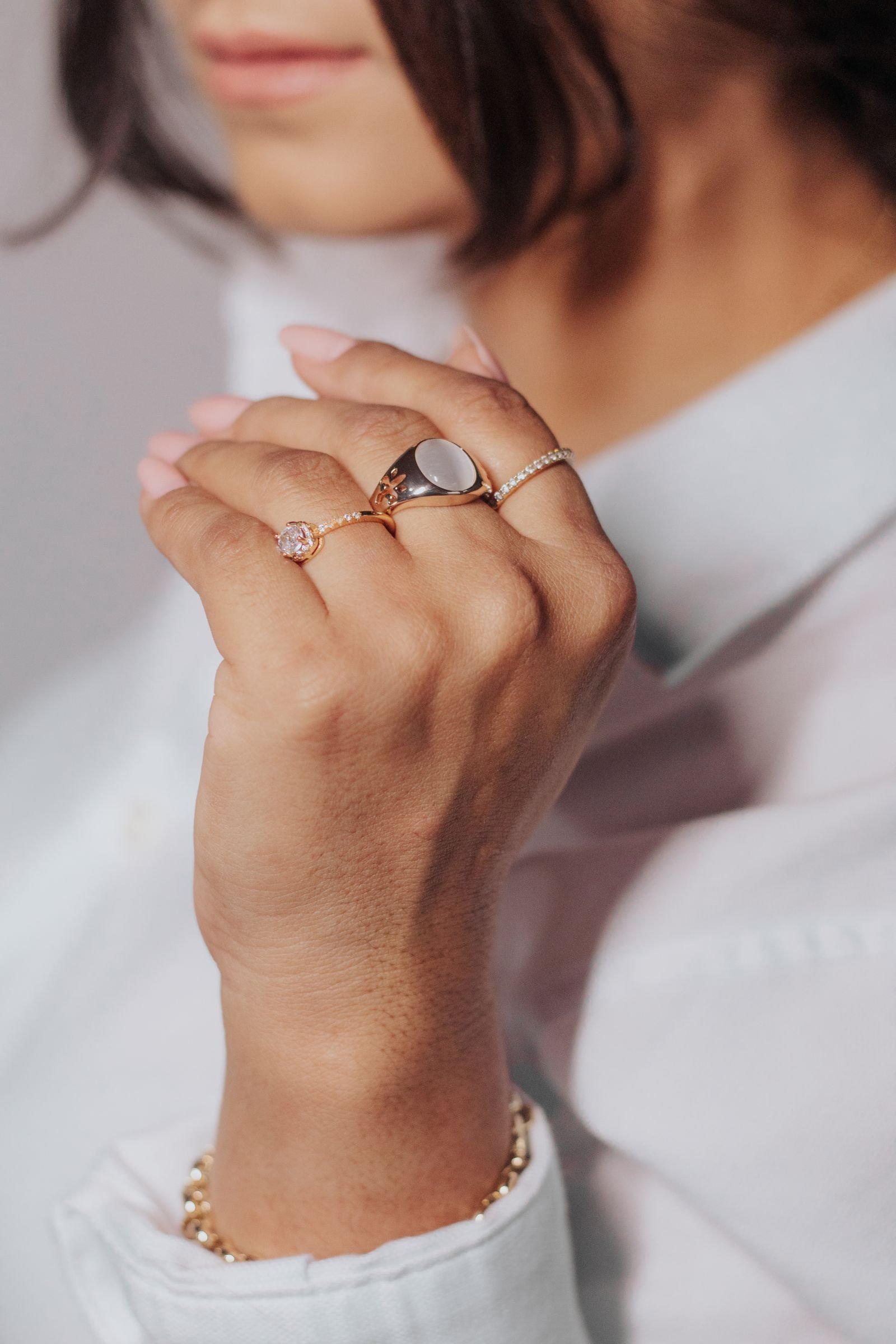 Anillos y pulsera de oro 18K combinados en la mano, estilo editorial elegante
