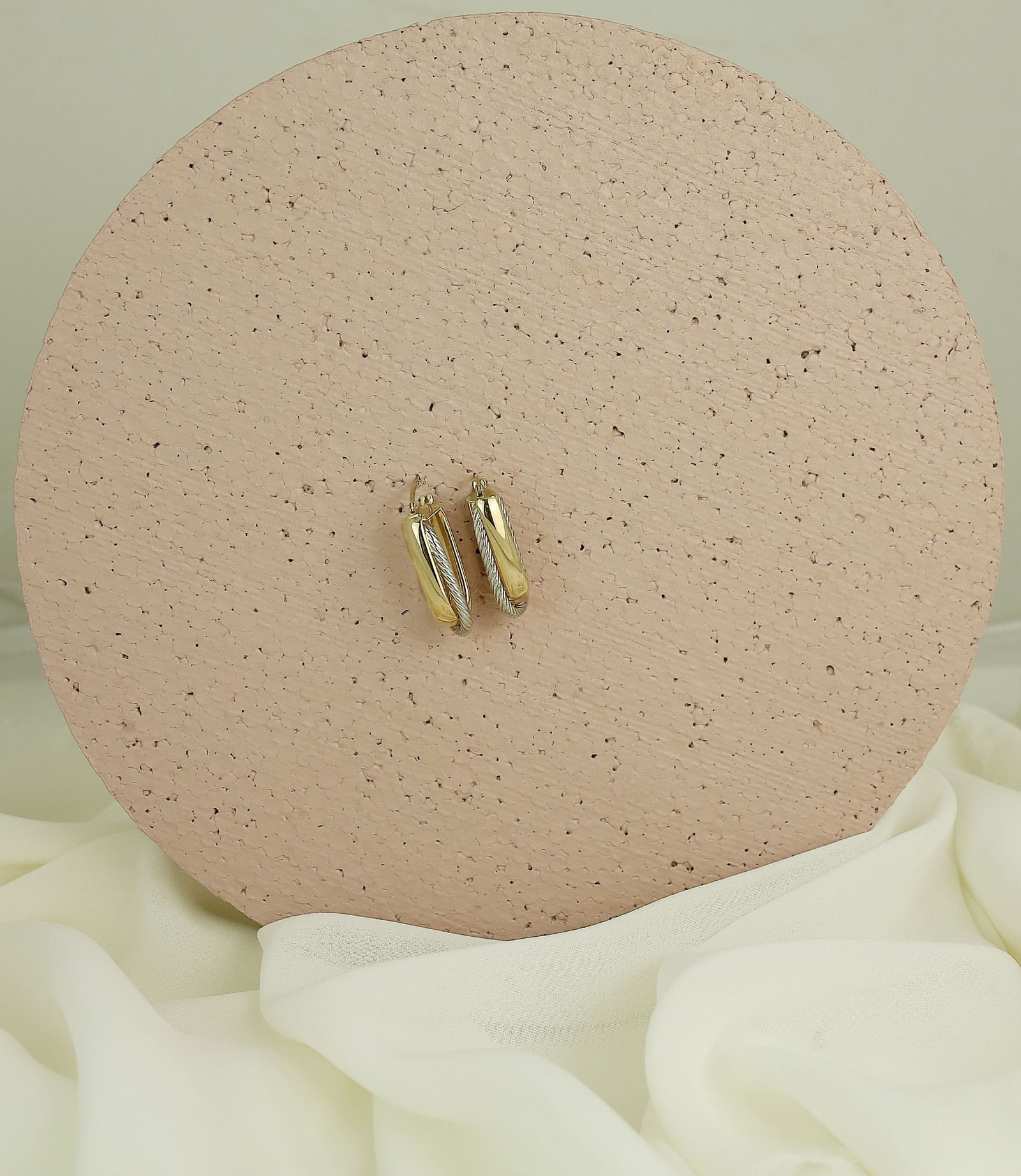 Aretes dorados minimalistas sobre superficie neutra, estilo editorial