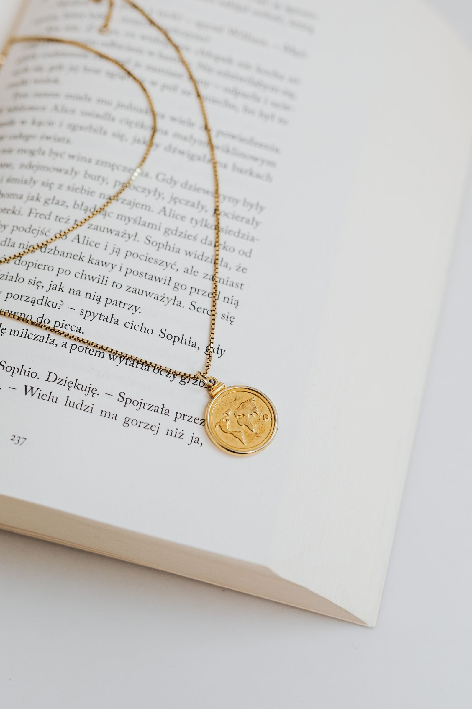 Dije de moneda en collar de oro 18K, composición editorial sobre libro