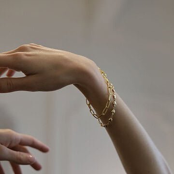 Pulsera de oro en la muñeca de mujer con cabello rizado.